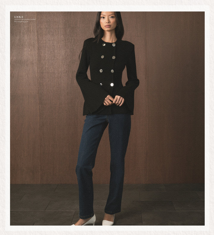 Woman wearing a black jacket with silver buttons and blue jeans against a brown background